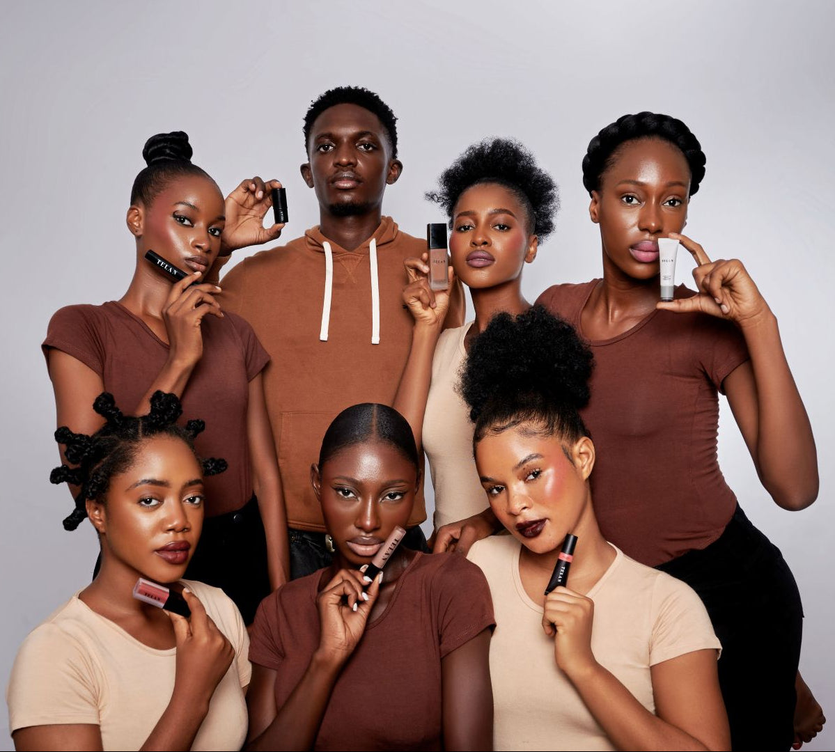 Group of people holding makeup products against a plain background